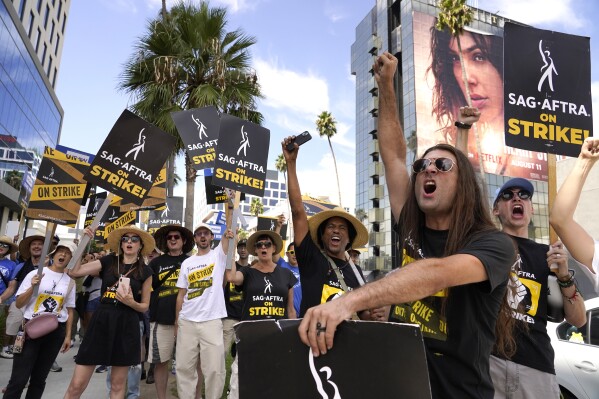 SAG-AFTRA member John Schmitt, second from right, and others carry signs on the picket line outside Netflix on Wednesday, Sept. 27, 2023, in Los Angeles. Hollywood's writers strike was declared over Tuesday night when board members from their union approved a contract agreement with studios, bringing the industry at least partly back from a historic halt in production. The actors strike continues in their bid to get better pay and working conditions. (AP Photo/Chris Pizzello)